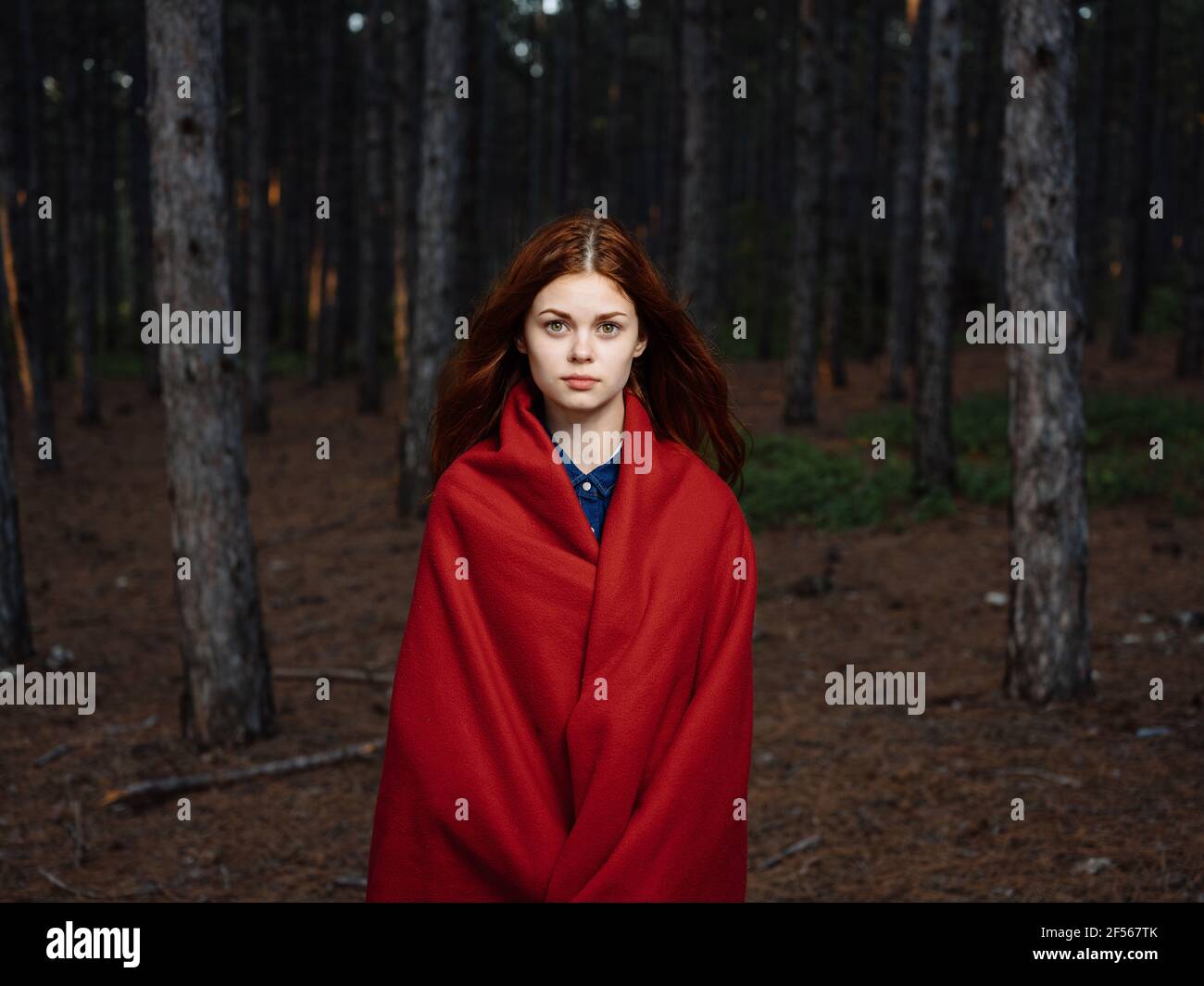 A red-haired woman with a plaid on her shoulders walks in the forest ...