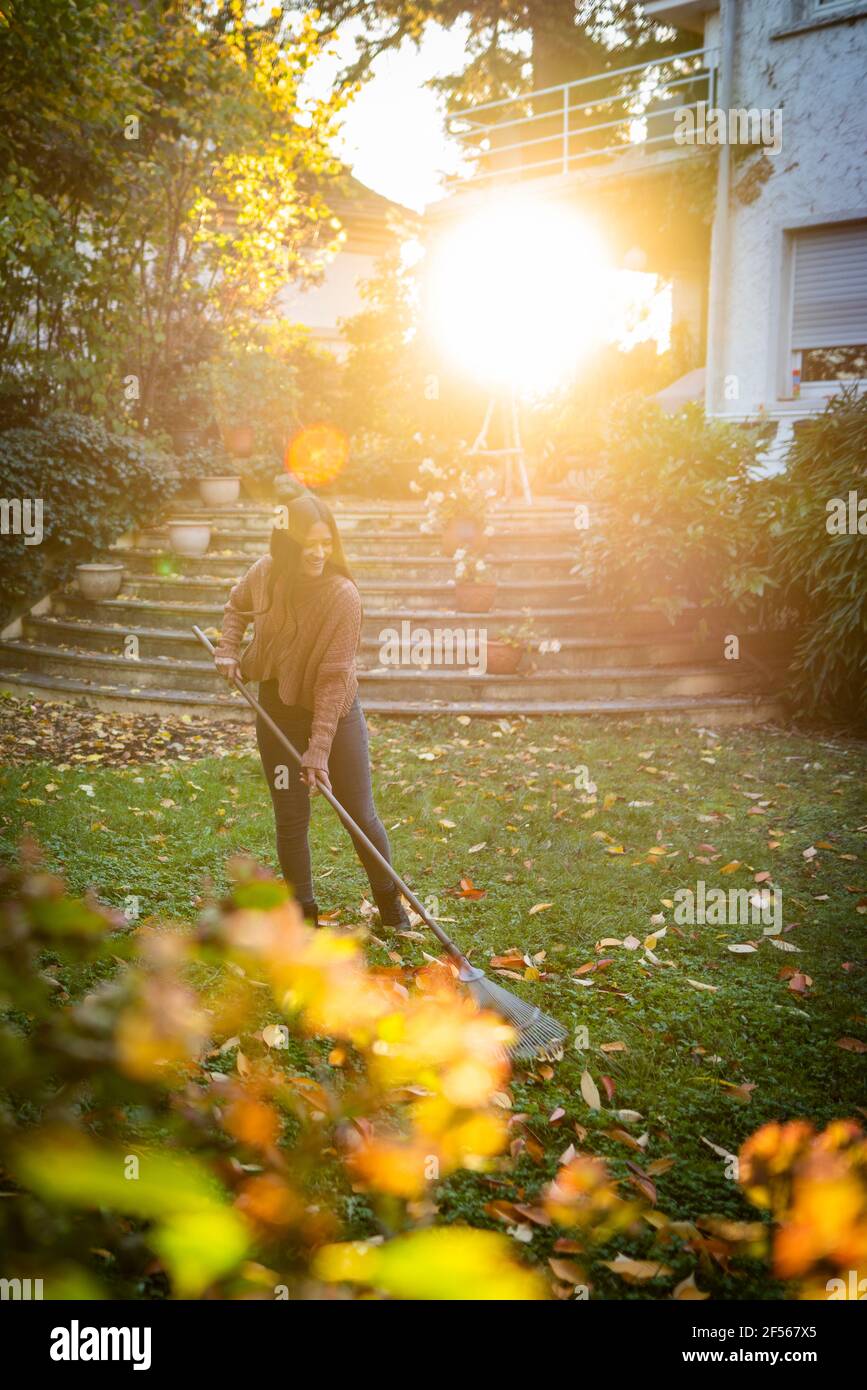 Woman sweeping with broom in garden on sunny day Stock Photo