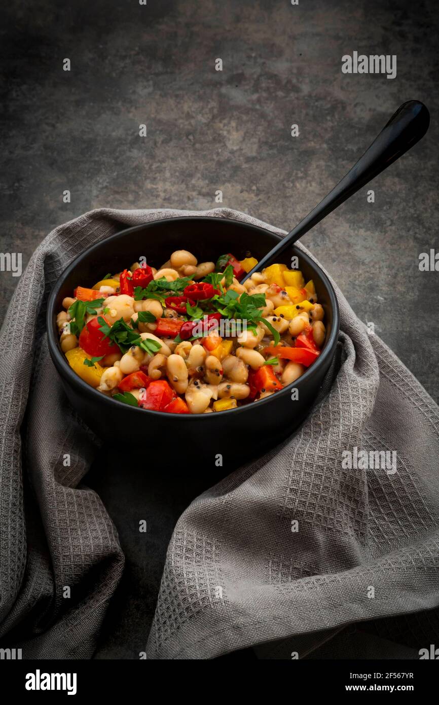 Studio shot of bowl of bean stew with bell and chili peppers, quinoa and parsley Stock Photo