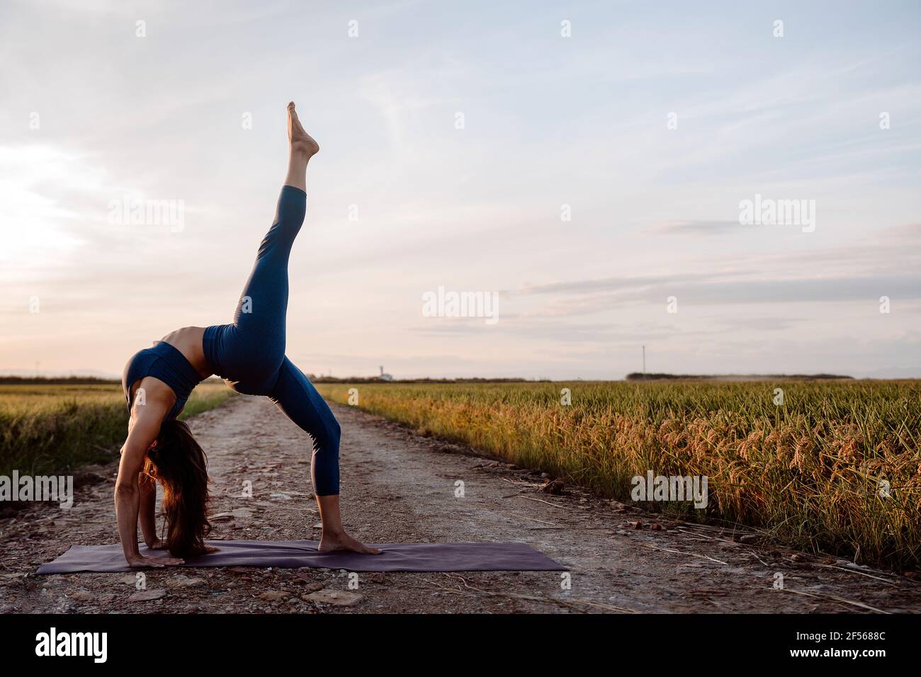 Woman doing back bend with one leg raised against sky Stock Photo