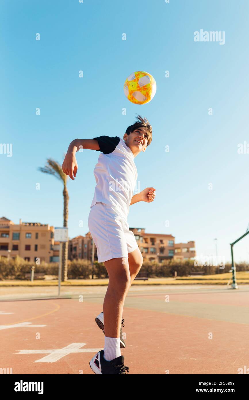 Boy heading soccer ball on sports court against sky Stock Photo