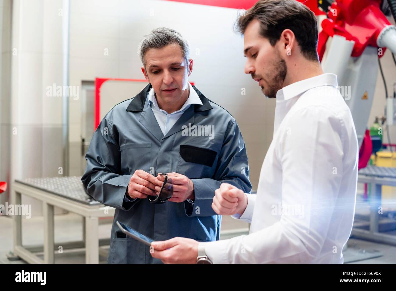 Male engineer using digital tablet while discussing with worker in factory Stock Photo