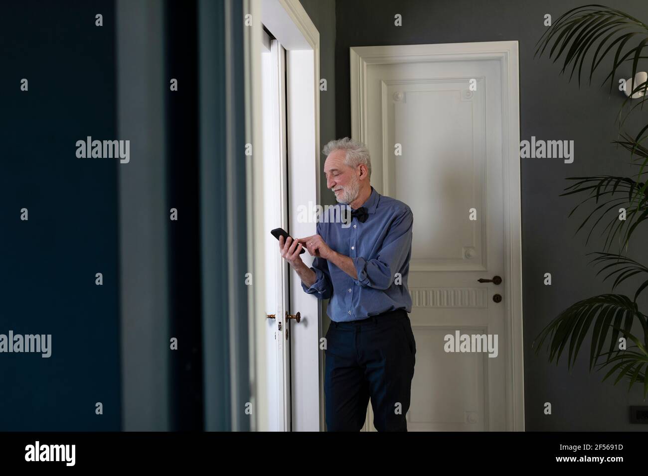 Senior man using phone while standing by window at home Stock Photo