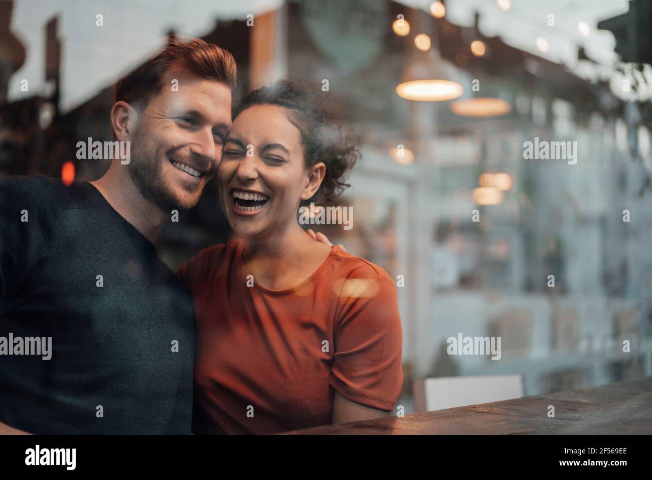 Happy couple laughing while sitting by table at cafe Stock Photo