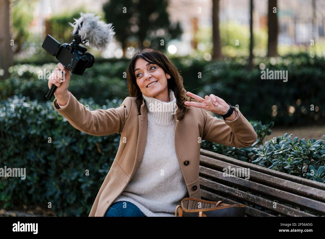 Smiling woman gesturing peace sign while taking selfie through camera at park Stock Photo