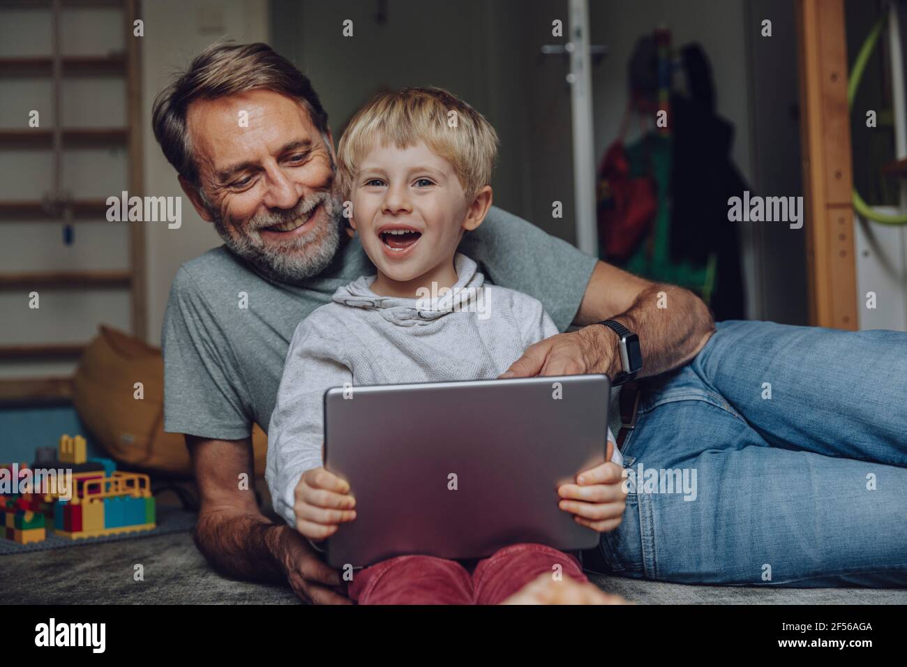 Smiling father and son using tablet in bedroom Stock Photo