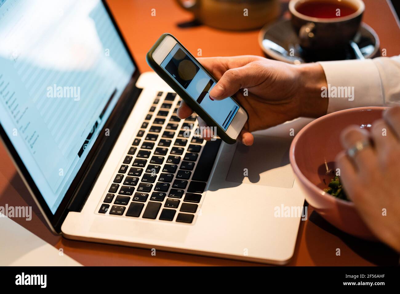 Businessman using smart phone over laptop while sitting at cafe Stock Photo