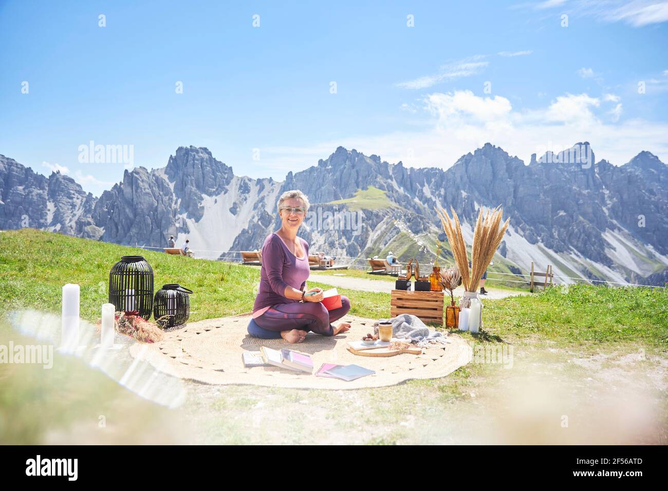 Smiling woman with book sitting on carpet against mountain Stock Photo