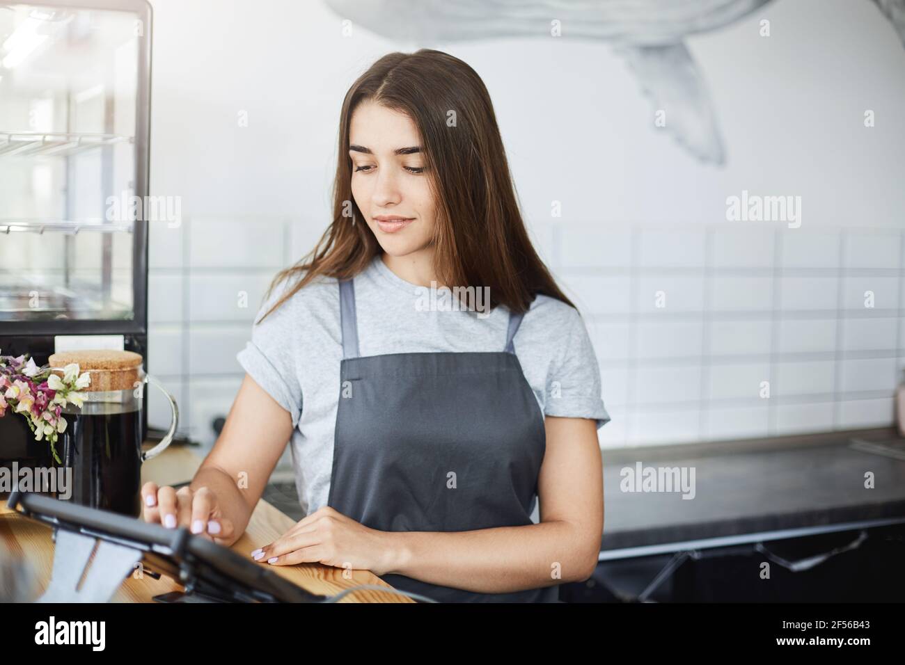 Portrait of beautiful long haired girl barista using a point of sale to run her successful coffee store business. Stock Photo