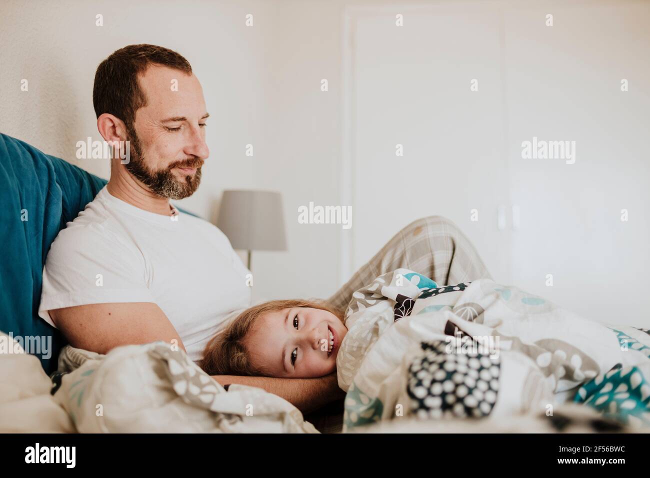 Father kissing daughter on forehead while son laughing on bed at home Stock Photo