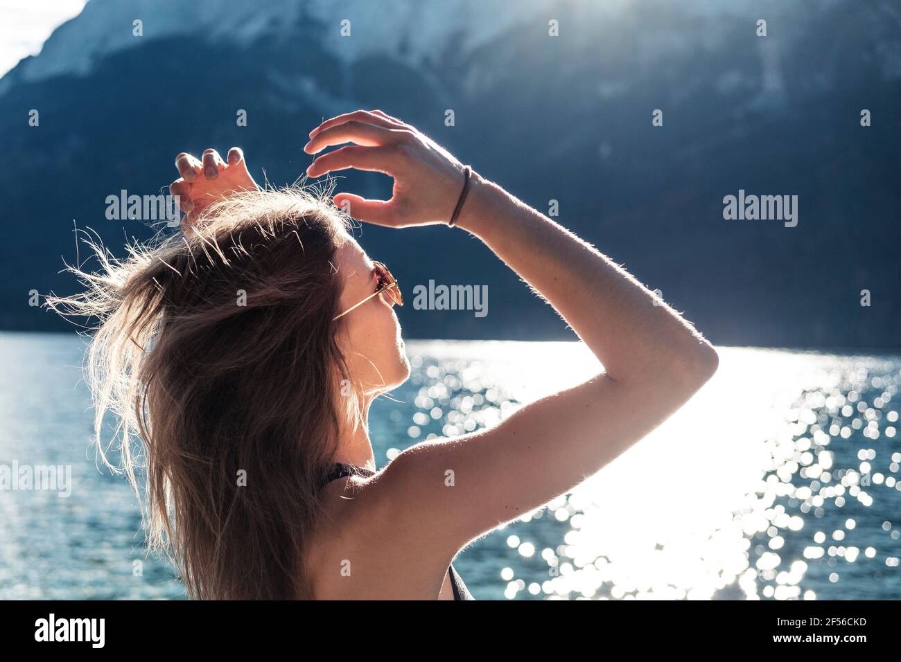 Woman with arms raised looking at view at Eibsee lake during sunny day Stock Photo