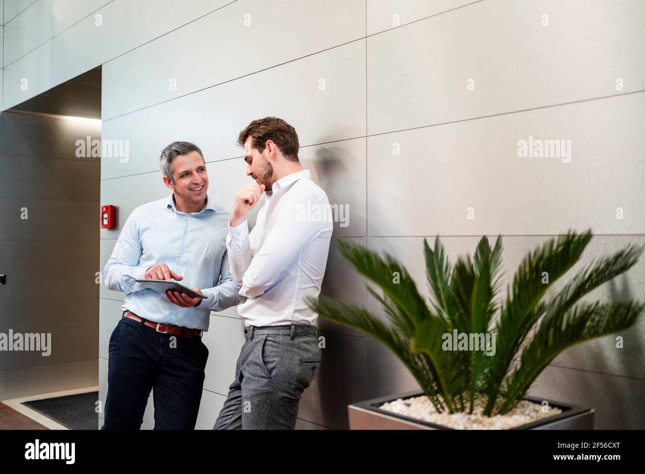 Smiling engineers using digital tablet while leaning on wall in factory Stock Photo