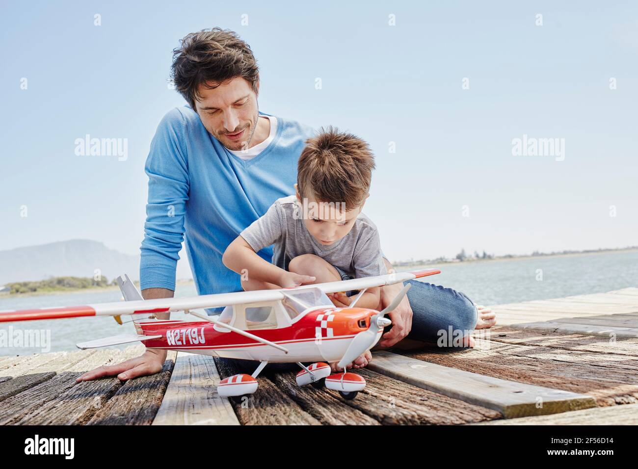Boy checking toy airplane while sitting on pier Stock Photo