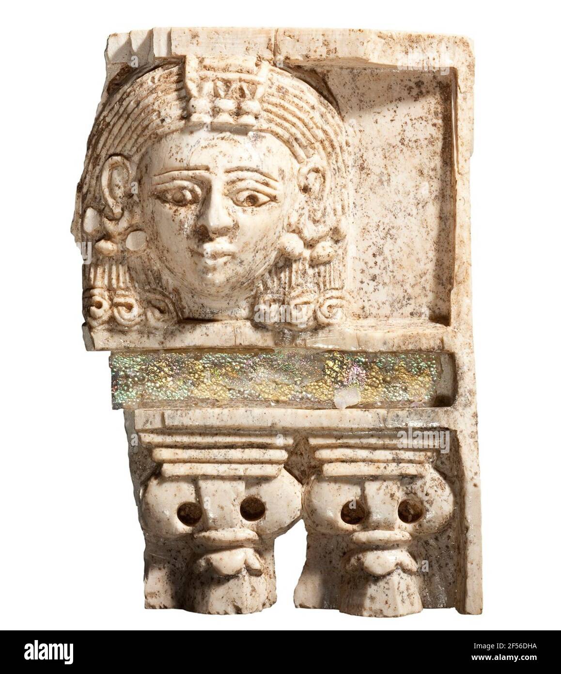 Furniture fitting 'Woman in the window'. A Women's Head of Egyptian Fashion, equipped with rich head and earmle jewelry, looks down from a rectangular window above a column balustrade. The hair, falling behind the ears on both sides, ends in curls shortly under chin height. Over the forehead a piece of jewelry. Between the window and the column balustrade is a well-preserved rectangular glass insert, iridescent due to the ground storage. There are two columns capitals to see with wide-deposing volutes and leaf robbery on slim column shafts. The cover plate is staging. The relief is on the left Stock Photo