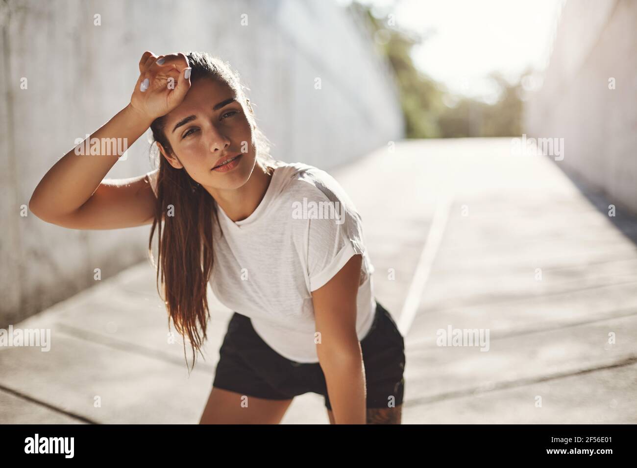 Sport, urban fitness and workout concept. Fit female athlete feel slight fatigue after morning run, wipe sweat from forehead taking breath before next Stock Photo
