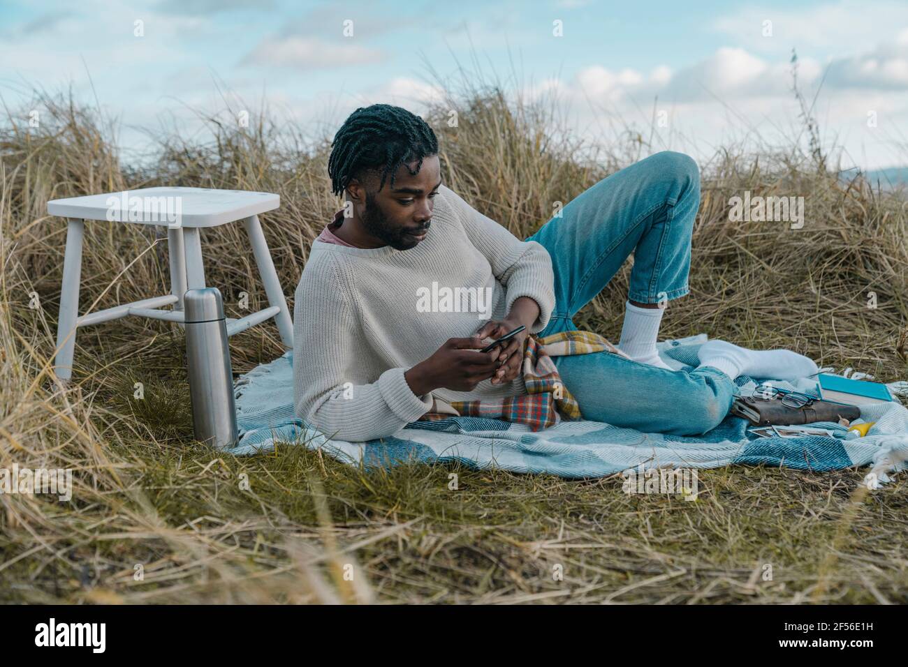 Young man using mobile while lying on blanket at beach Stock Photo