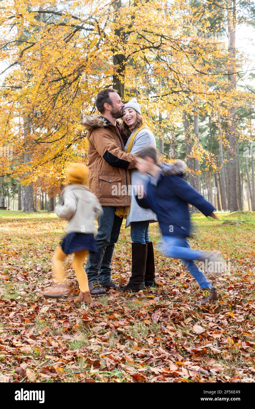 Man kissing woman while standing with children playing around in forest Stock Photo