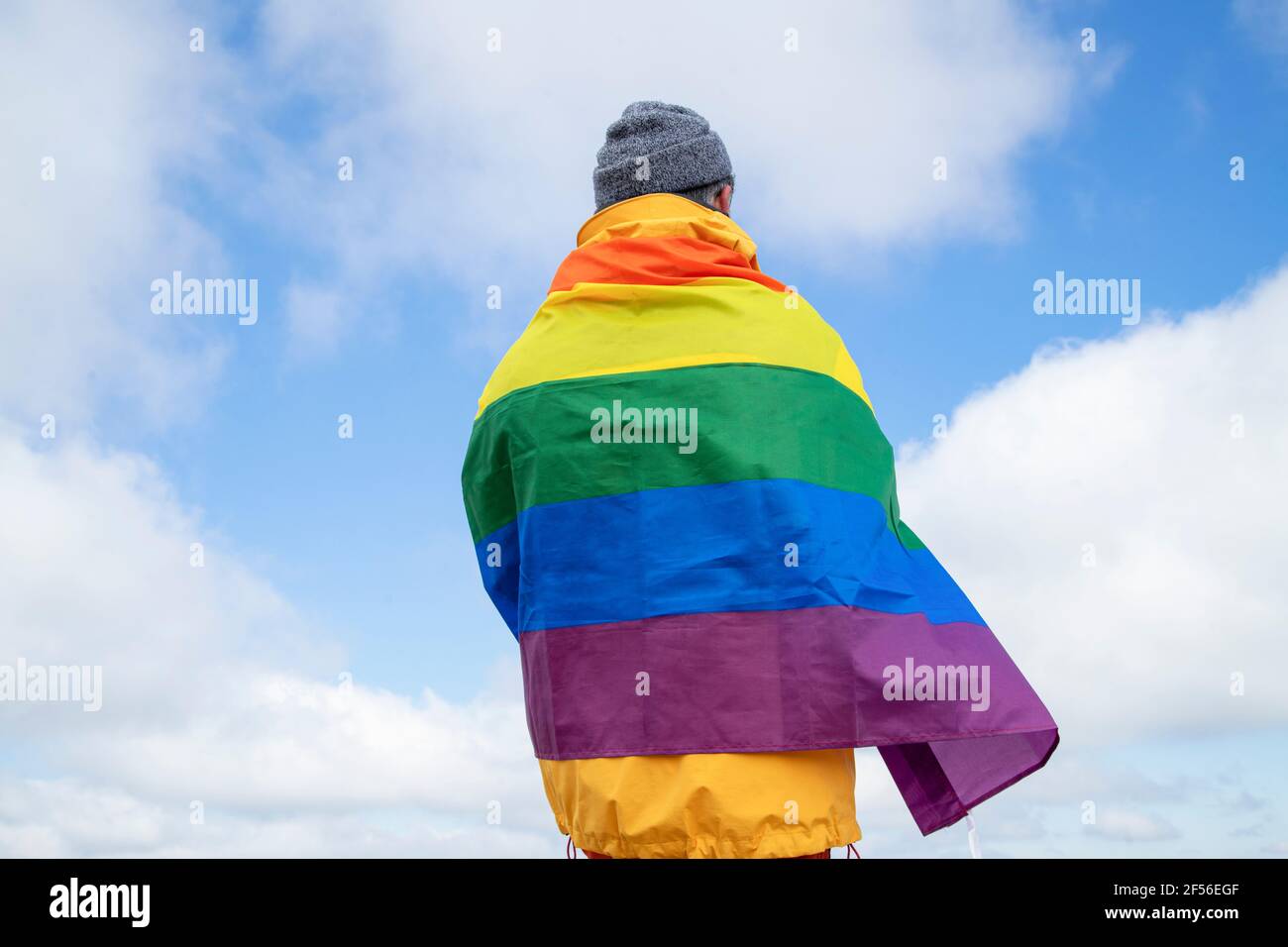 Rear view of a man standing on top of the hill with the LGBT pride flag Stock Photo