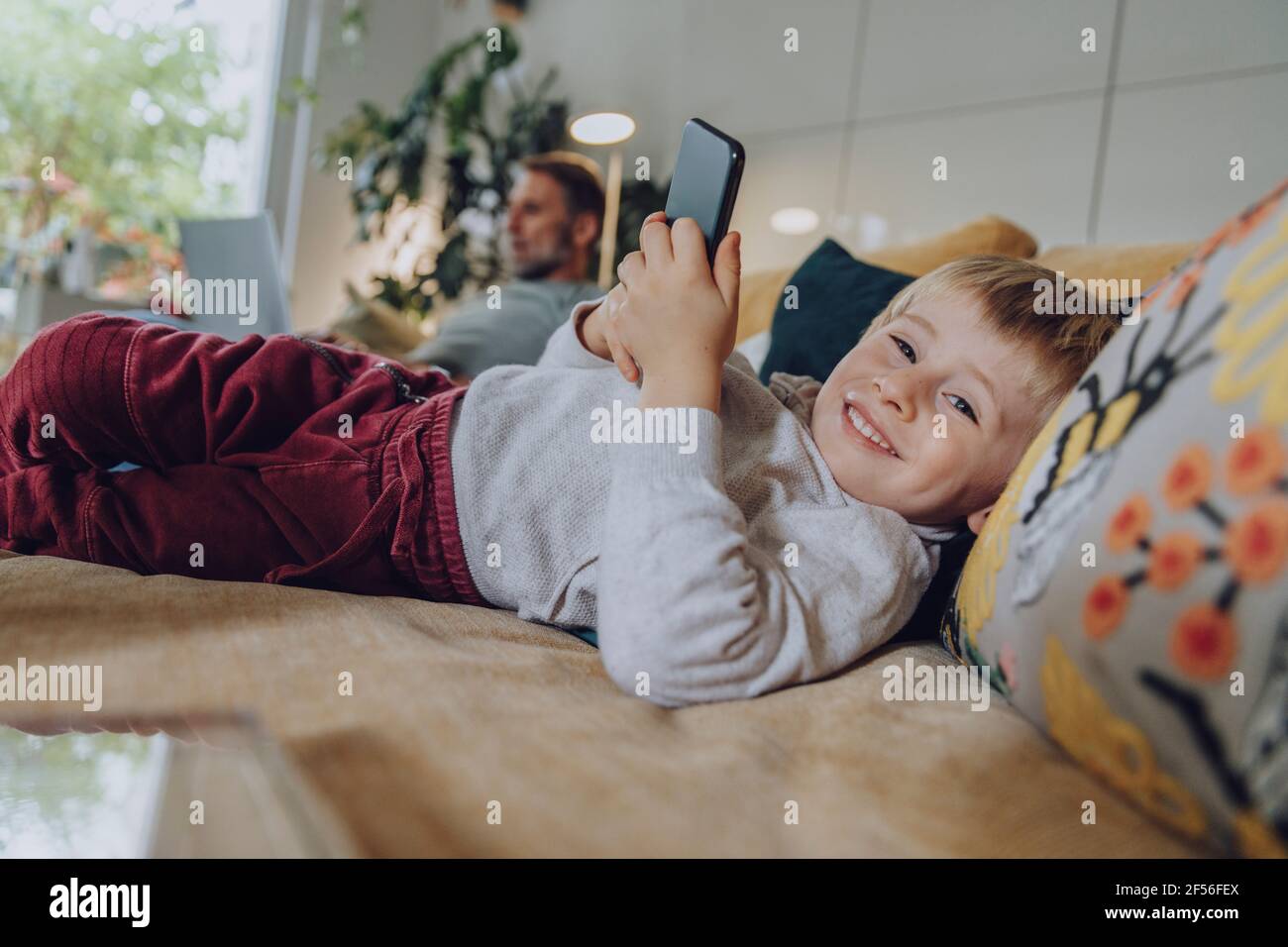 Smiling boy using mobile phone while lying on sofa at home Stock Photo
