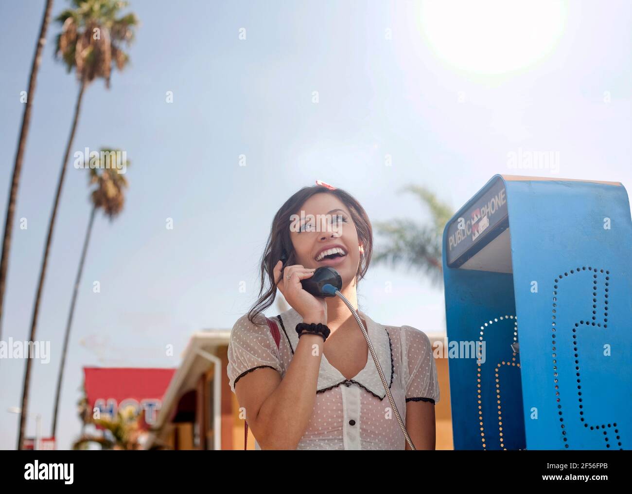 Young woman talking on pay phone while standing against sky Stock Photo