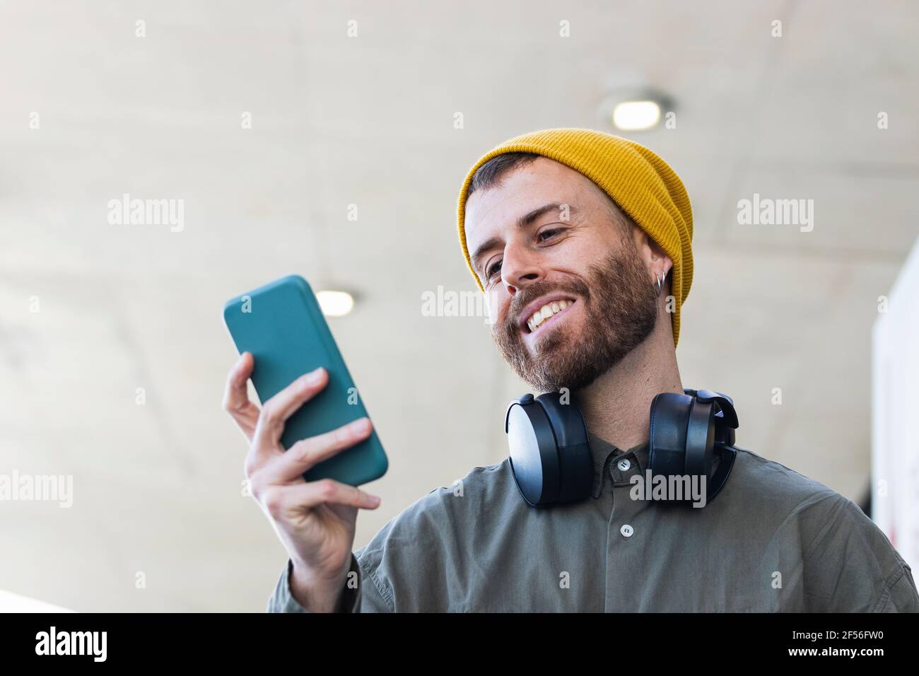Smiling man with knit hat using smart phone while standing outdoors Stock Photo