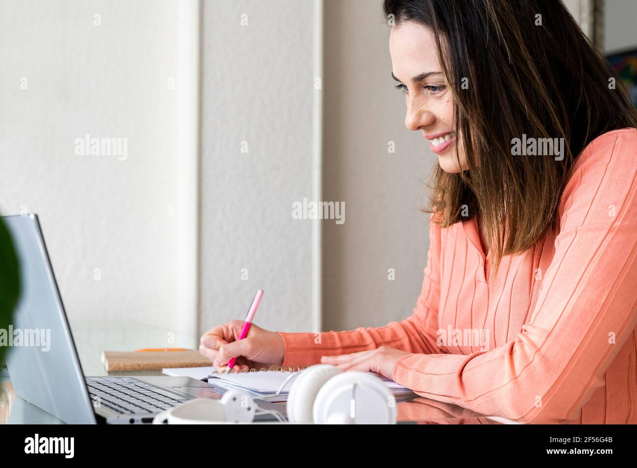 Smiling female entrepreneur writing in diary during video call at home office Stock Photo