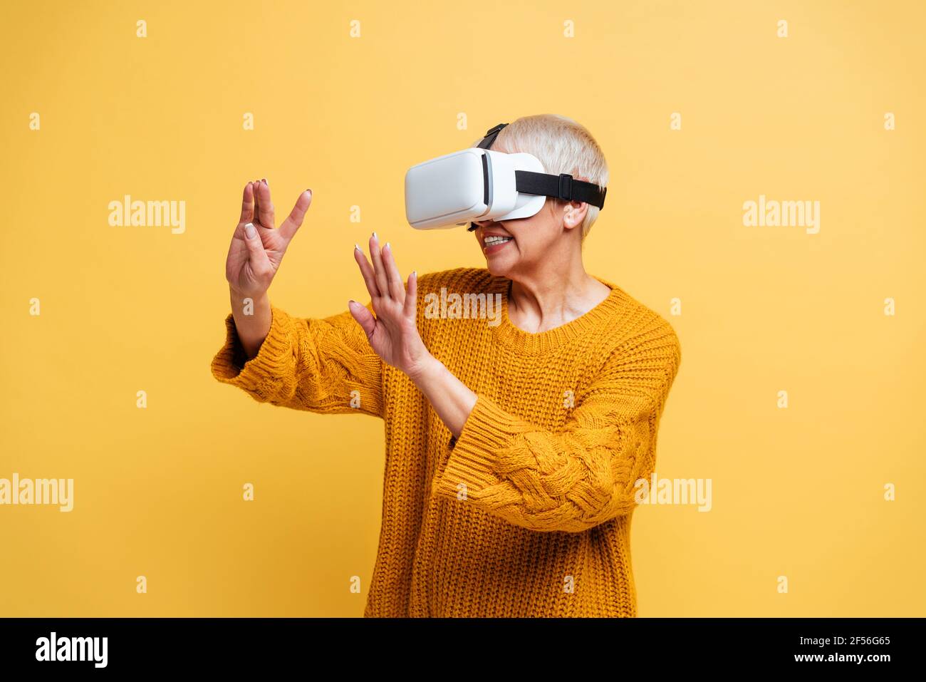 Woman gesturing while using virtual reality headset standing against yellow background Stock Photo
