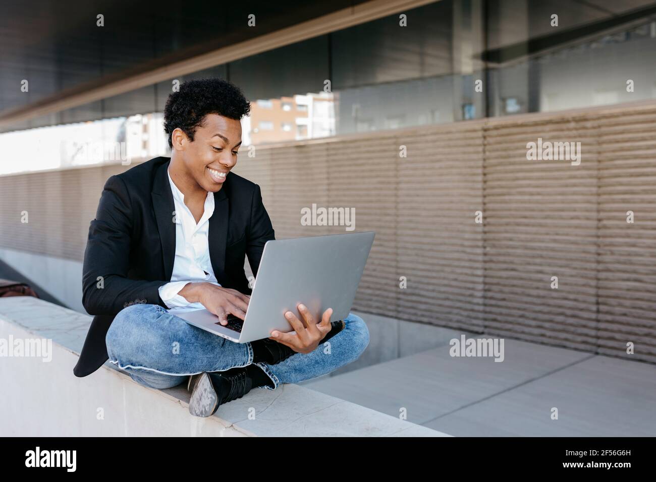Smiling businessman using laptop while sitting cross legged on ...
