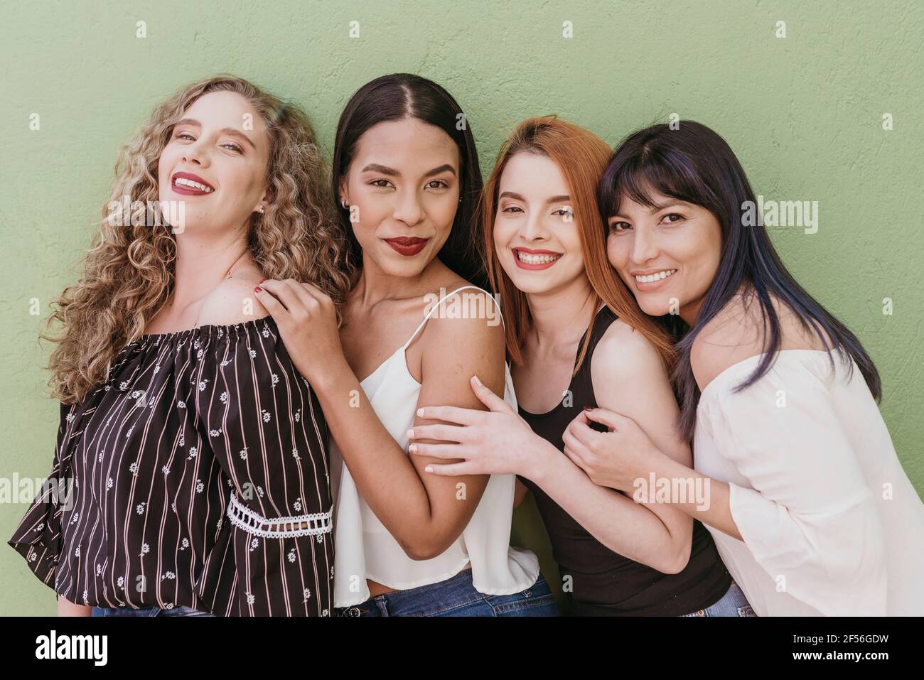 Happy multi ethnic friends standing against green wall Stock Photo