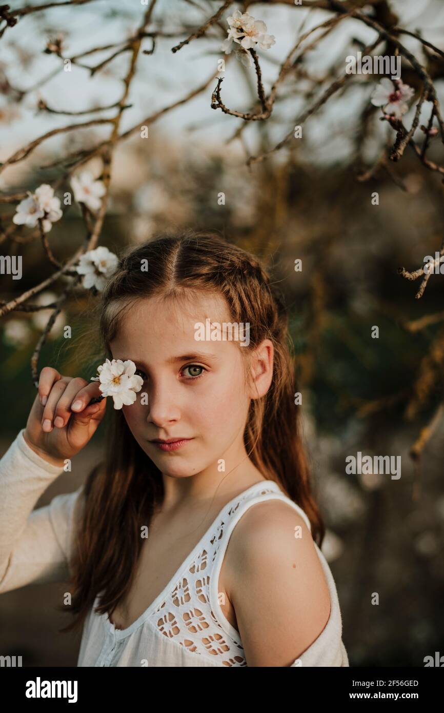 Cute girl covering eye from branch of almond tree flower during ...
