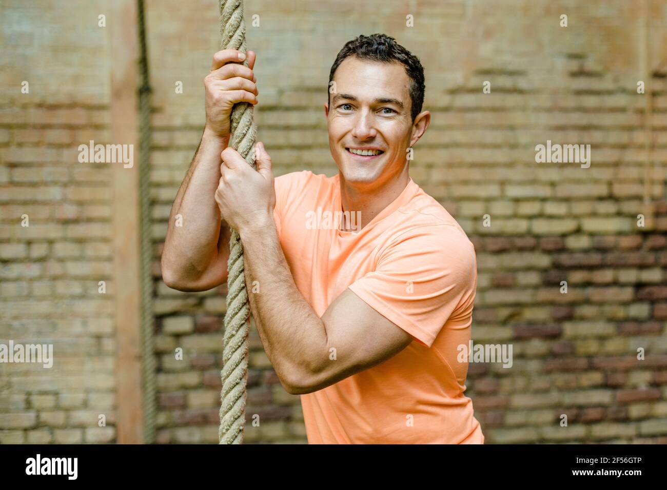 Handsome man holding rope against brick wall Stock Photo