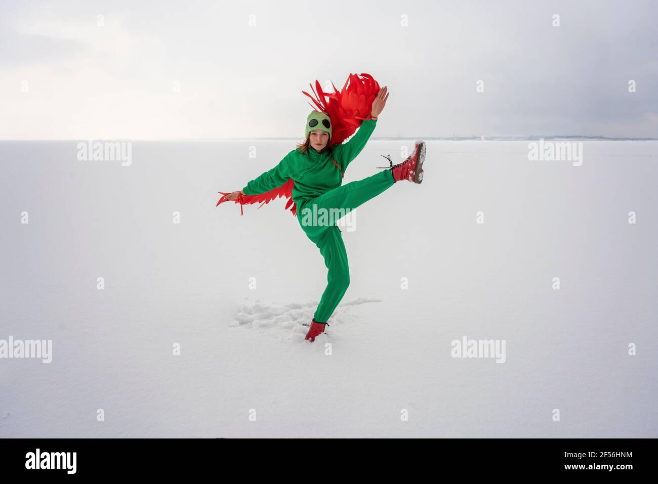 Woman in bird costume with leg up standing on snow against sky Stock Photo
