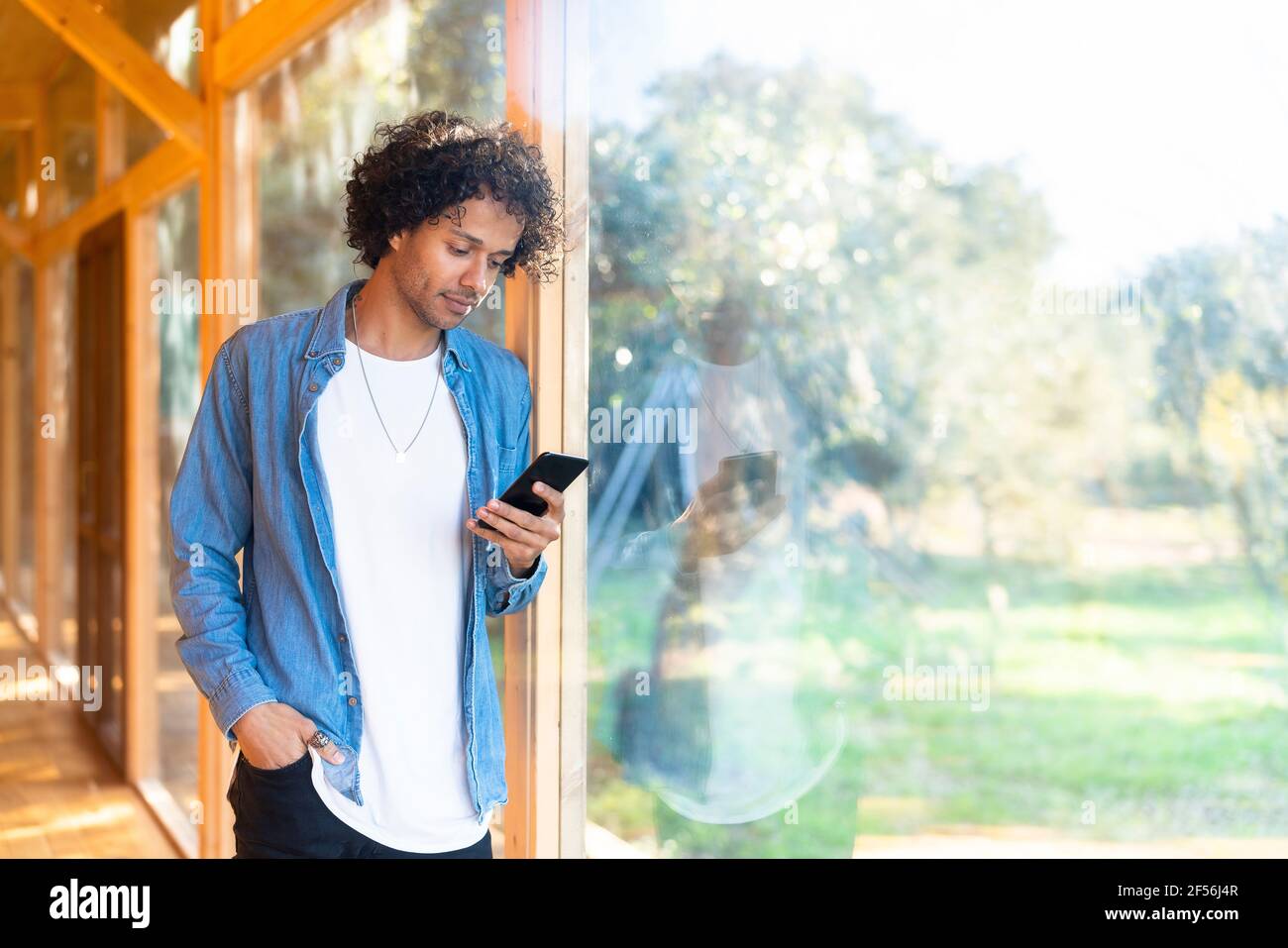 Young man using smart phone while standing at front yard window Stock Photo