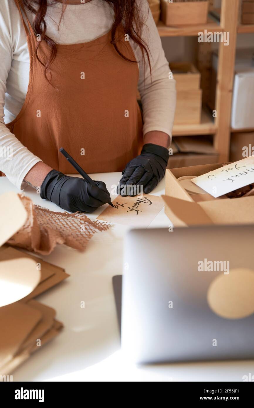 Female entrepreneur writing thank you note to put it in order packaging at workshop Stock Photo