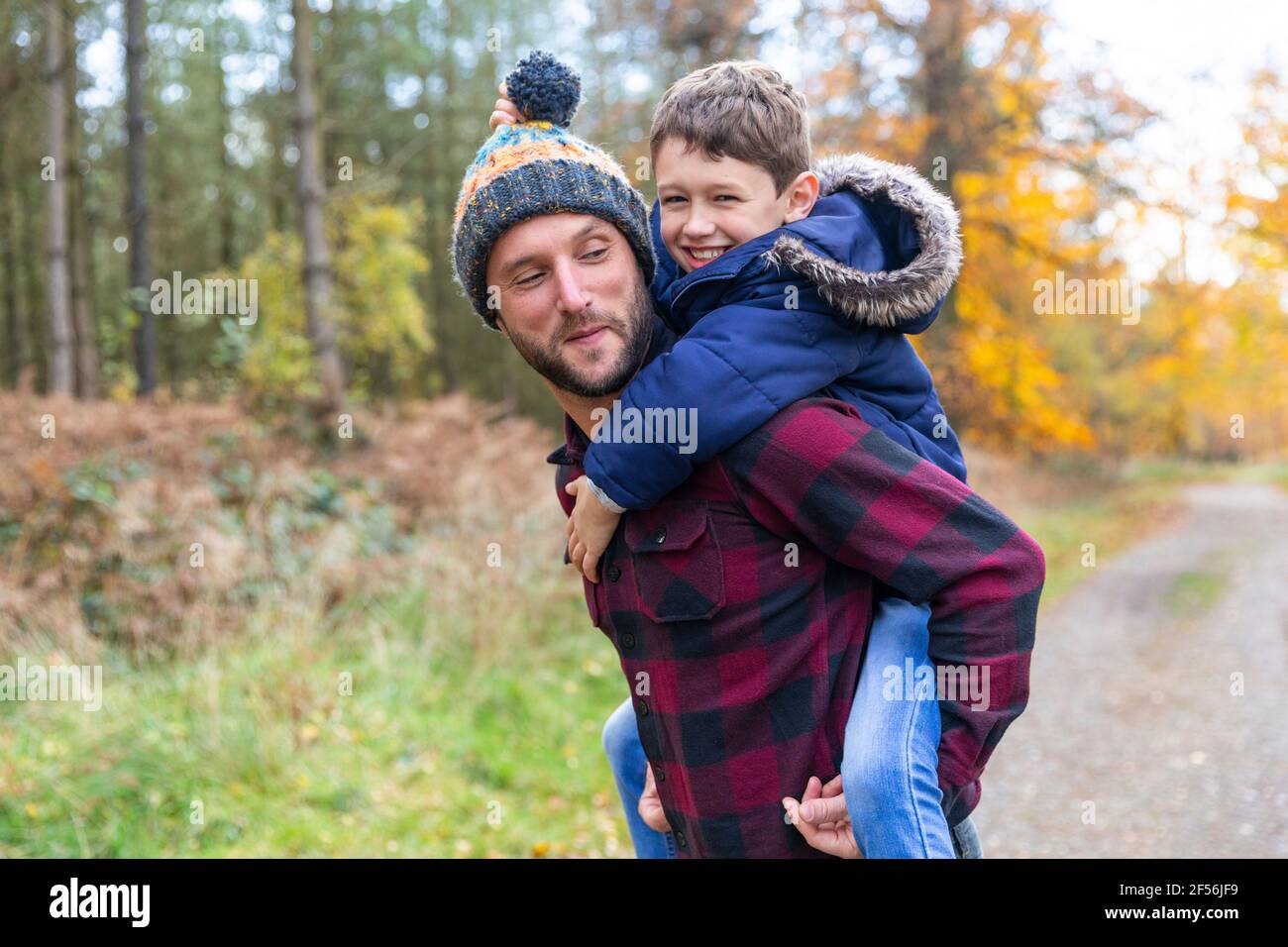 Smiling boy enjoying while piggybacking on father in forest Stock Photo