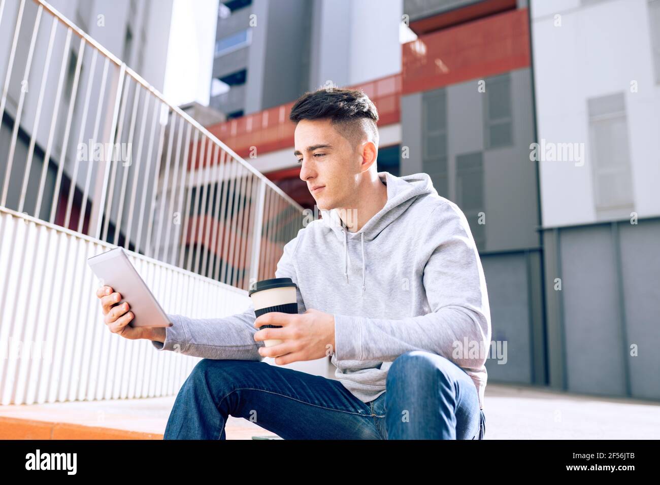 Young man holding reusable coffee cup while using digital tablet against building Stock Photo