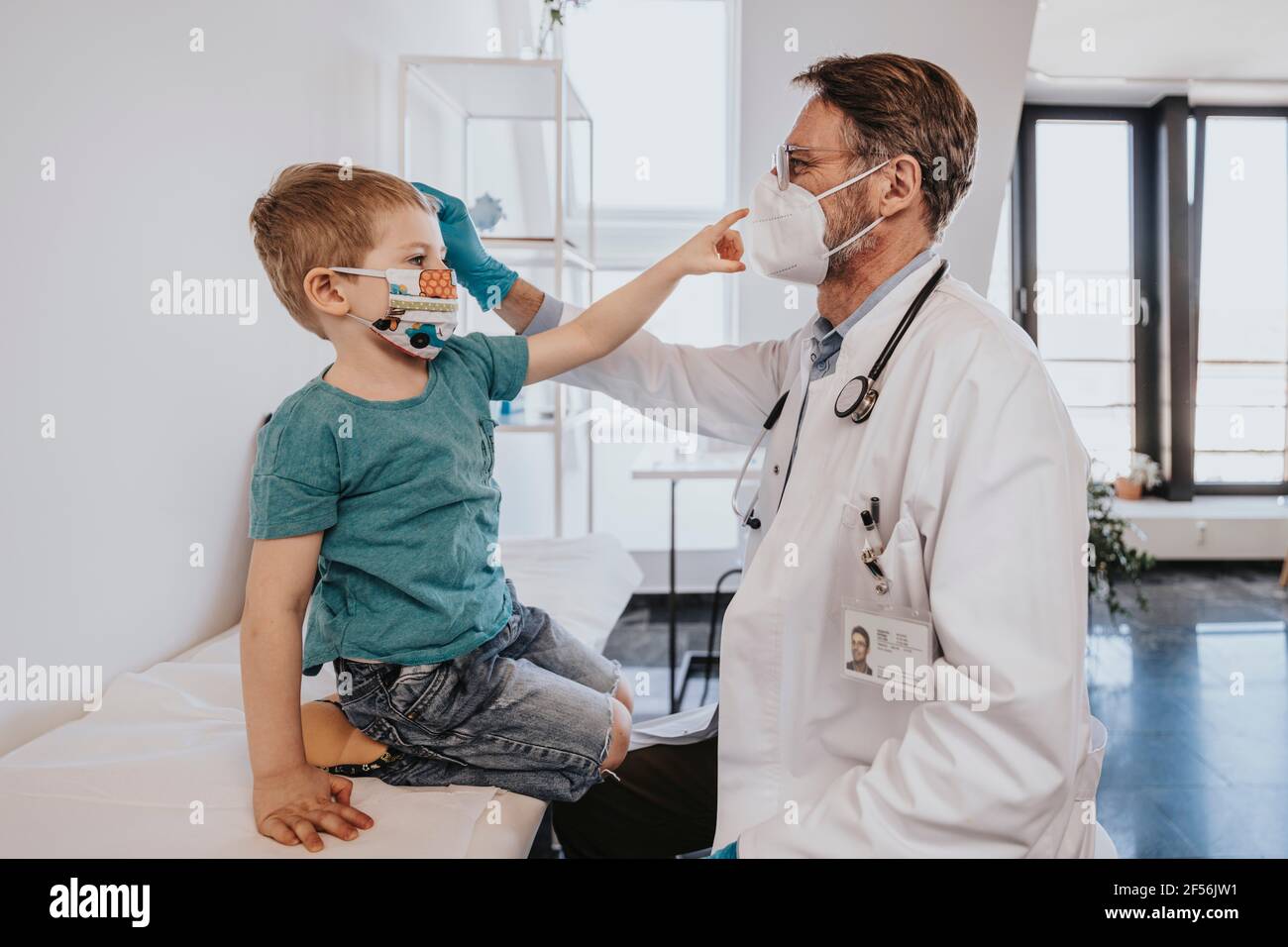 Male pediatrician with protective face mask checking boy in medical examination room Stock Photo