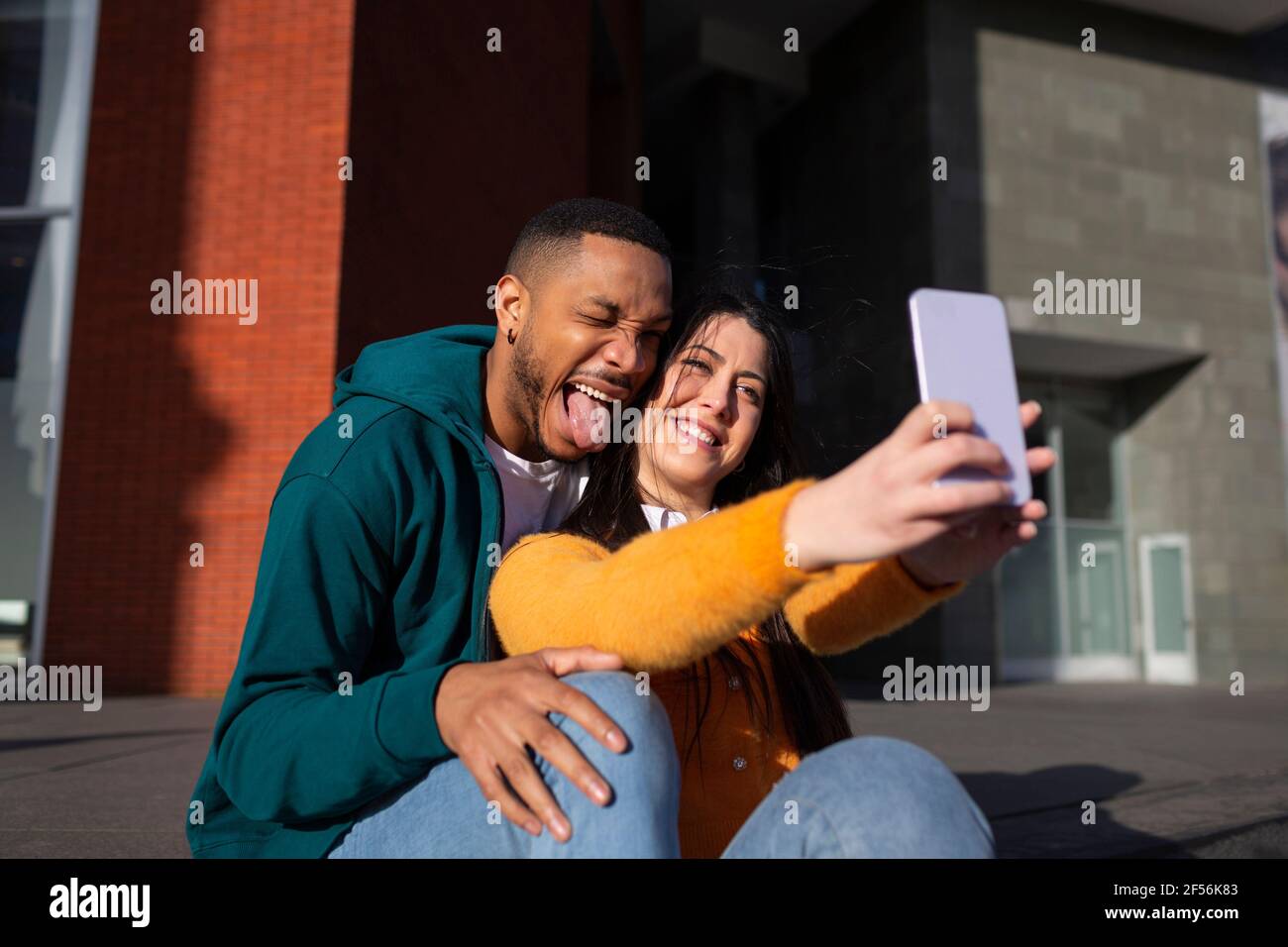 Young man making face while girlfriend taking selfie through smart phone Stock Photo
