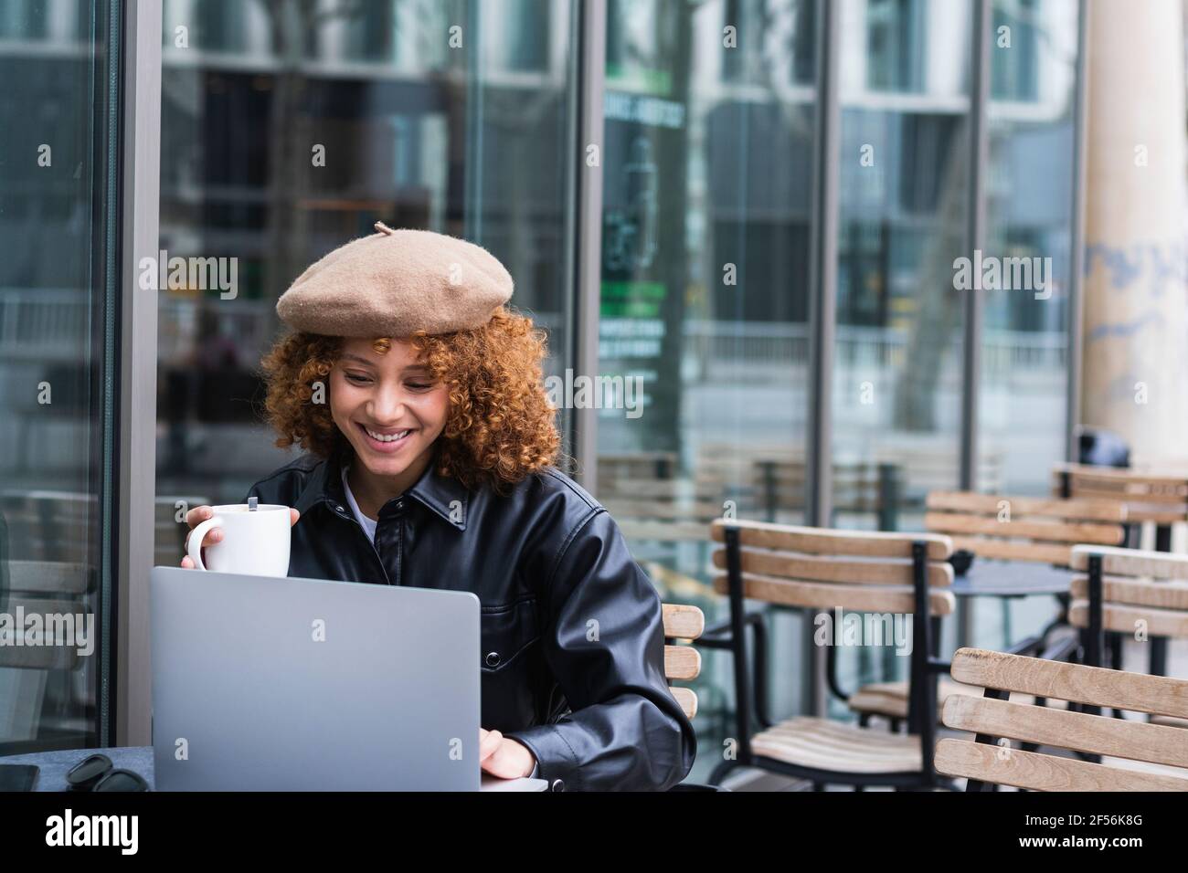 Female teenager with coffee cup using laptop at sidewalk cafe Stock Photo