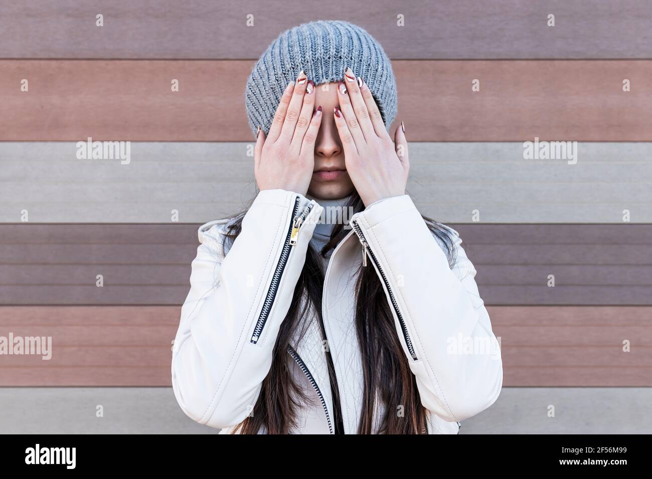 Teenage girl covering her face with hands while standing against wall ...