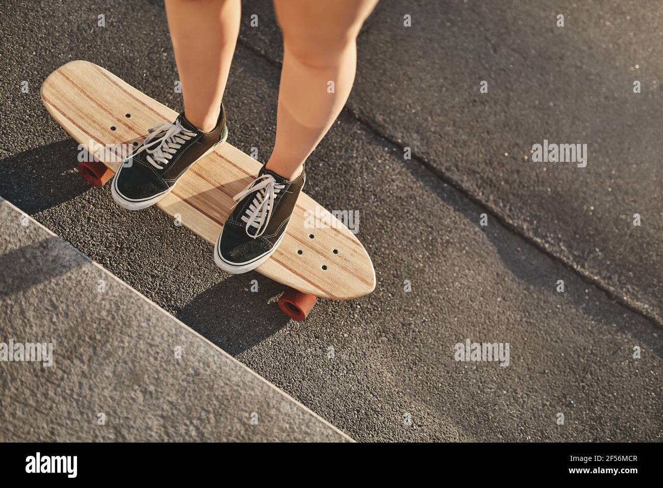 Upper-angle cropped shot caucasian woman hands in sneakers standing on wooden penny board, perform kickflip, learn how do tricks and stunts at Stock Photo