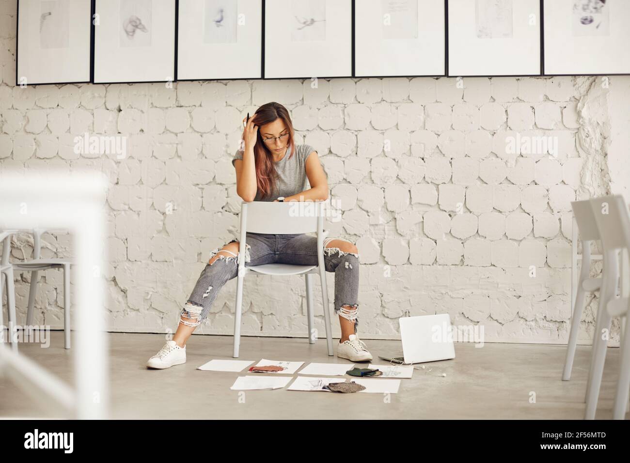 Aspiring fashion designer thinking of textile and sketches scattered on concrete floor in her