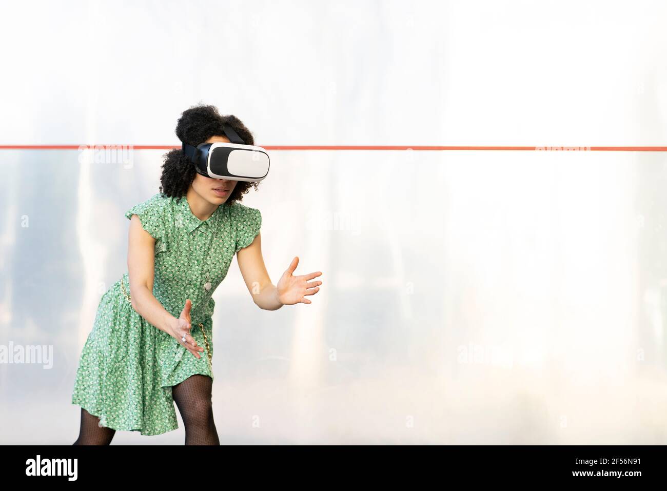 Young woman playing while wearing Virtual reality headset against wall Stock Photo
