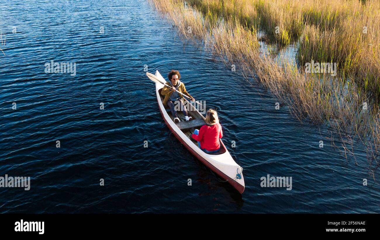 Man with oar paddling while sitting with woman in canoe on river Stock