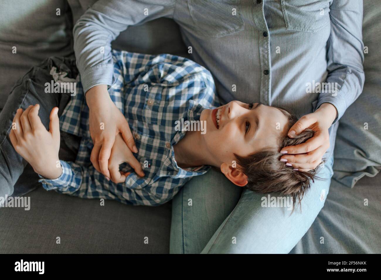 Careful mother stroking smiling boy lying down on lap at home Stock Photo