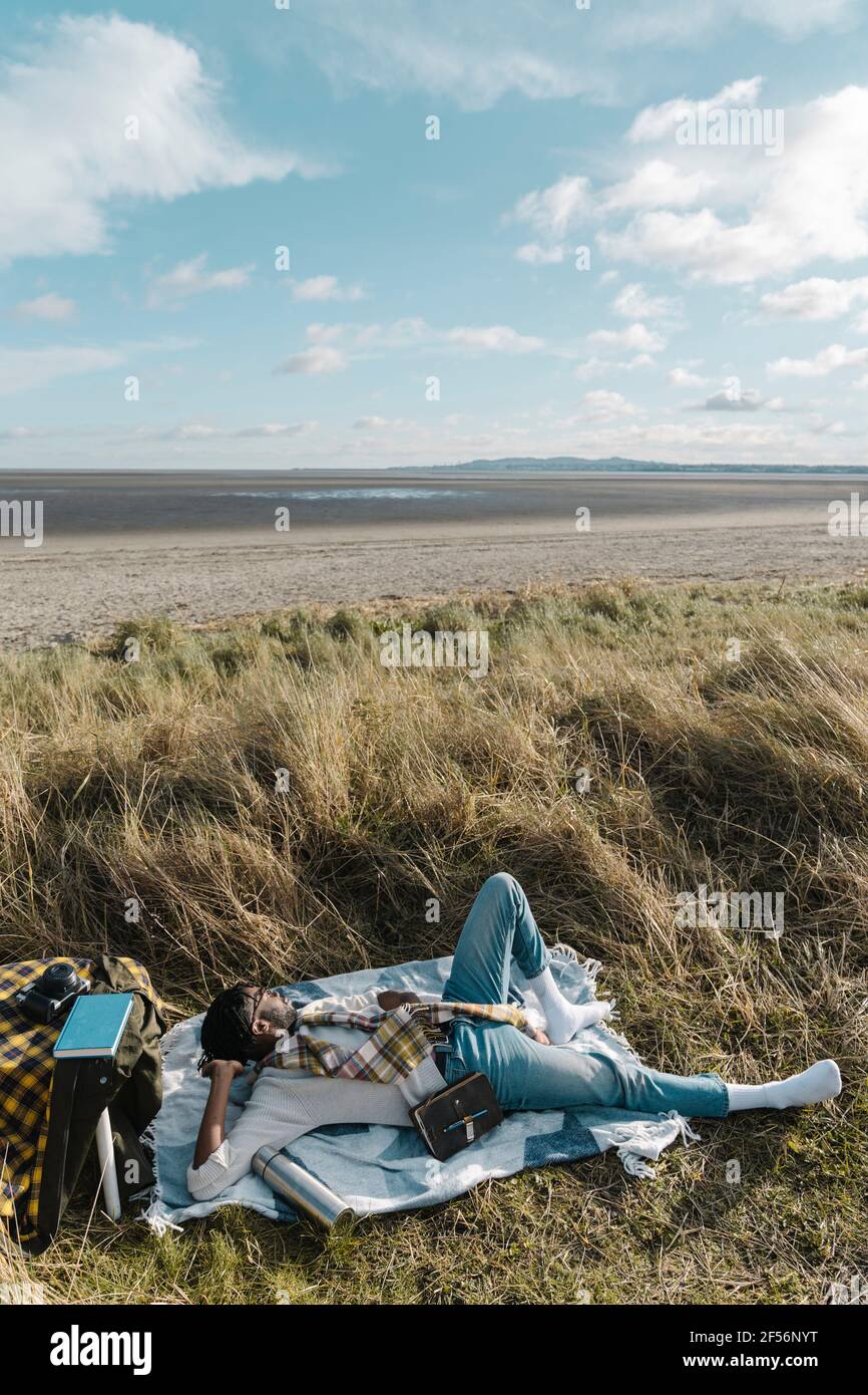 Young man lying on blanket while looking away at beach Stock Photo