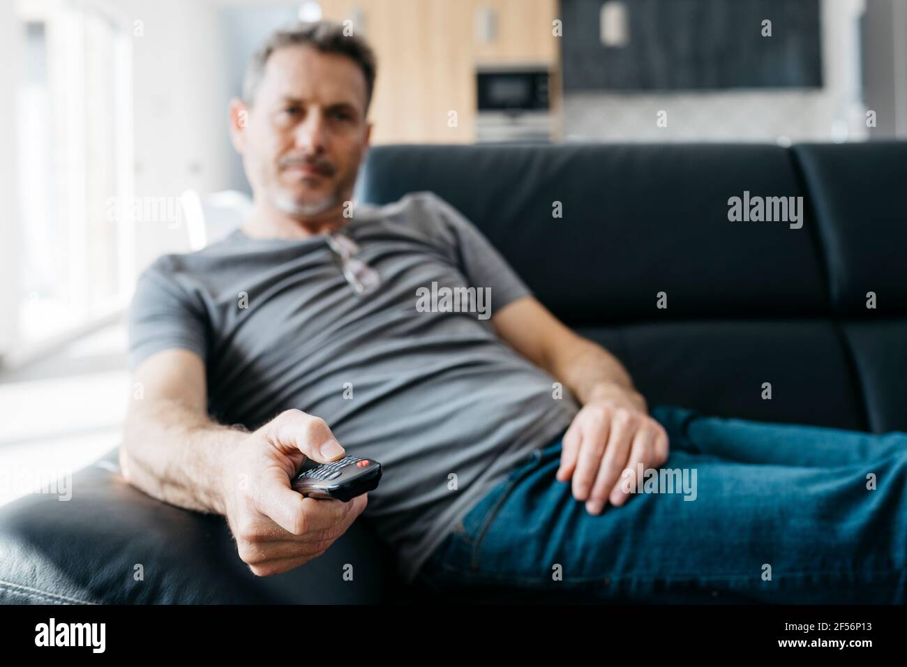 Mature man changing channels through remote control on sofa in living room Stock Photo