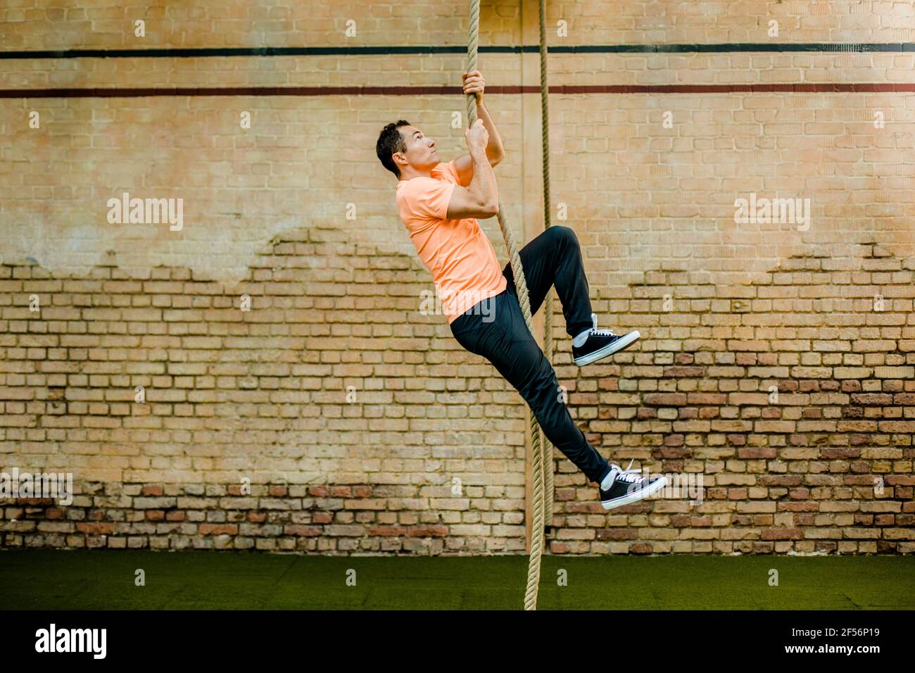 Man climbing on rope by brick wall at gym Stock Photo