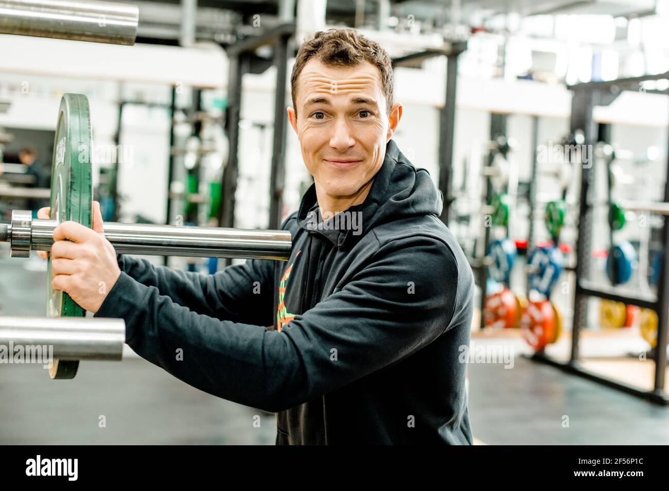 Smiling male athlete in sports clothing holding weights disc in gym Stock Photo