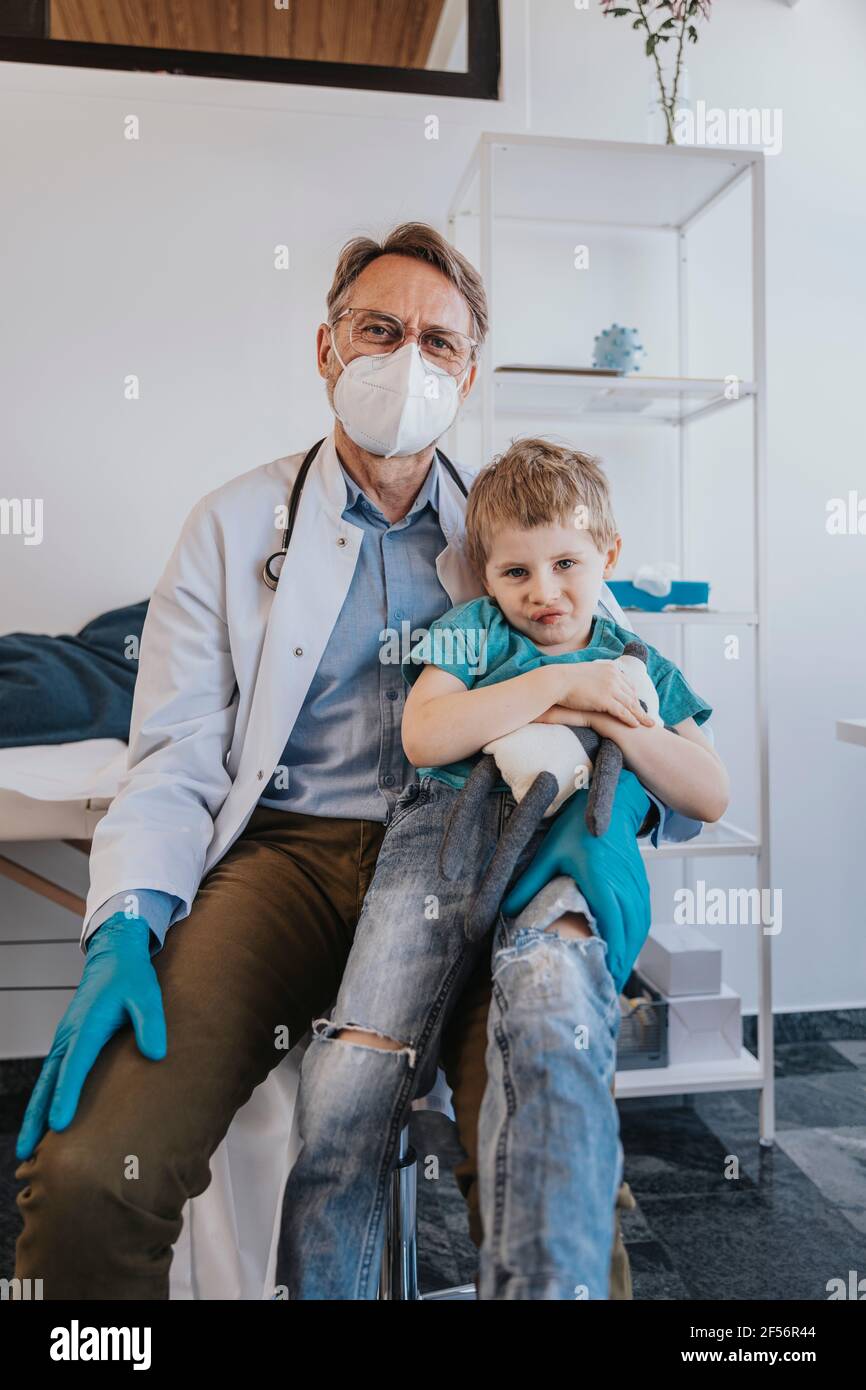 Pediatrician sitting with boy on lap at examination room Stock Photo